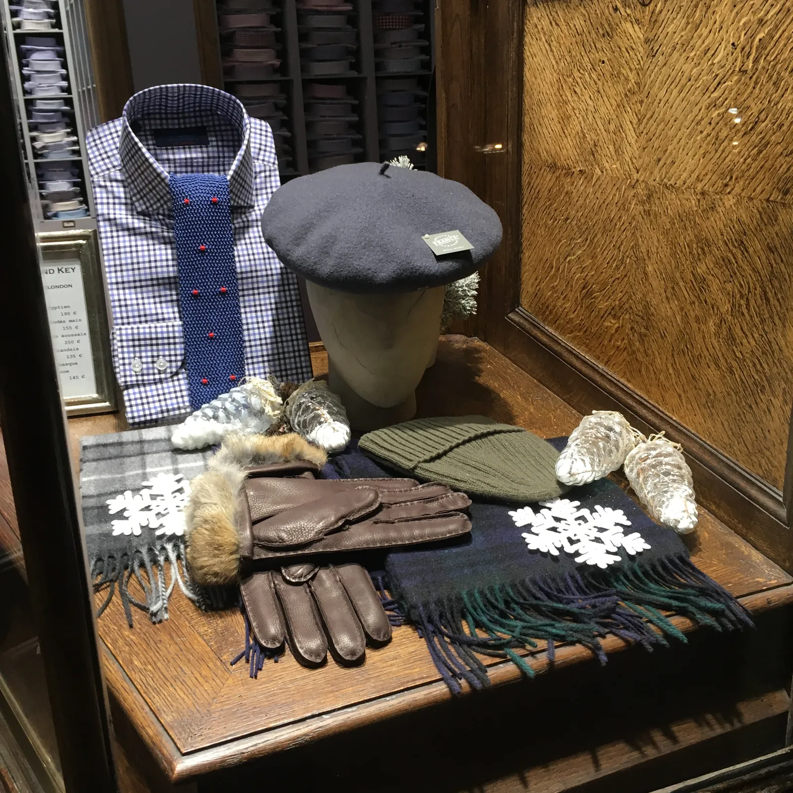 Composición de Navidad en una tienda de caballero con camisa, corbata, boina, guantes de piel, gorros de punto y copos de nieve blancos sobre una mesa de madera