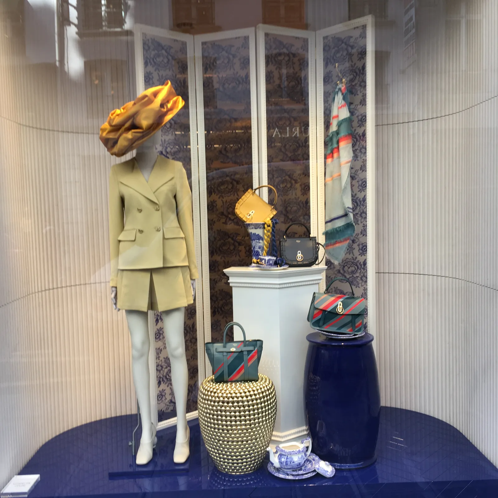 Escaparate de moda con maniquí en traje de chaqueta beige, bolsos y tocado dorado