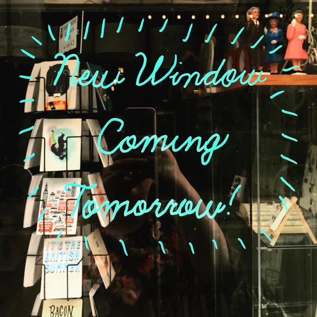 Cristal de escaparate con el mensaje New Window Coming Tomorrow escrito en letras turquesa y la tienda detrás