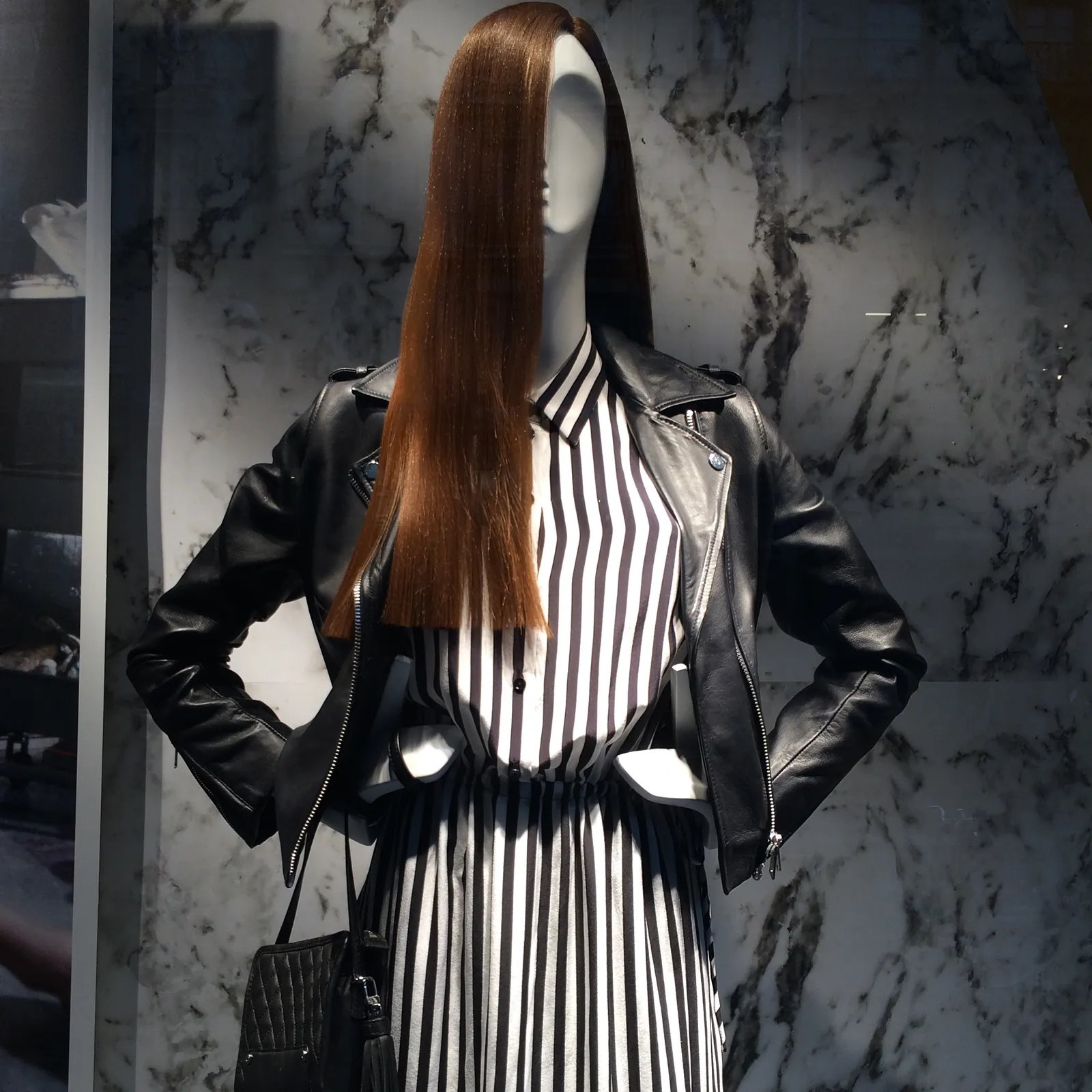 Maniquí con cazadora de cuero negra y vestido de rayas blancas y negras ante un fondo de mármol gris en un escaparate