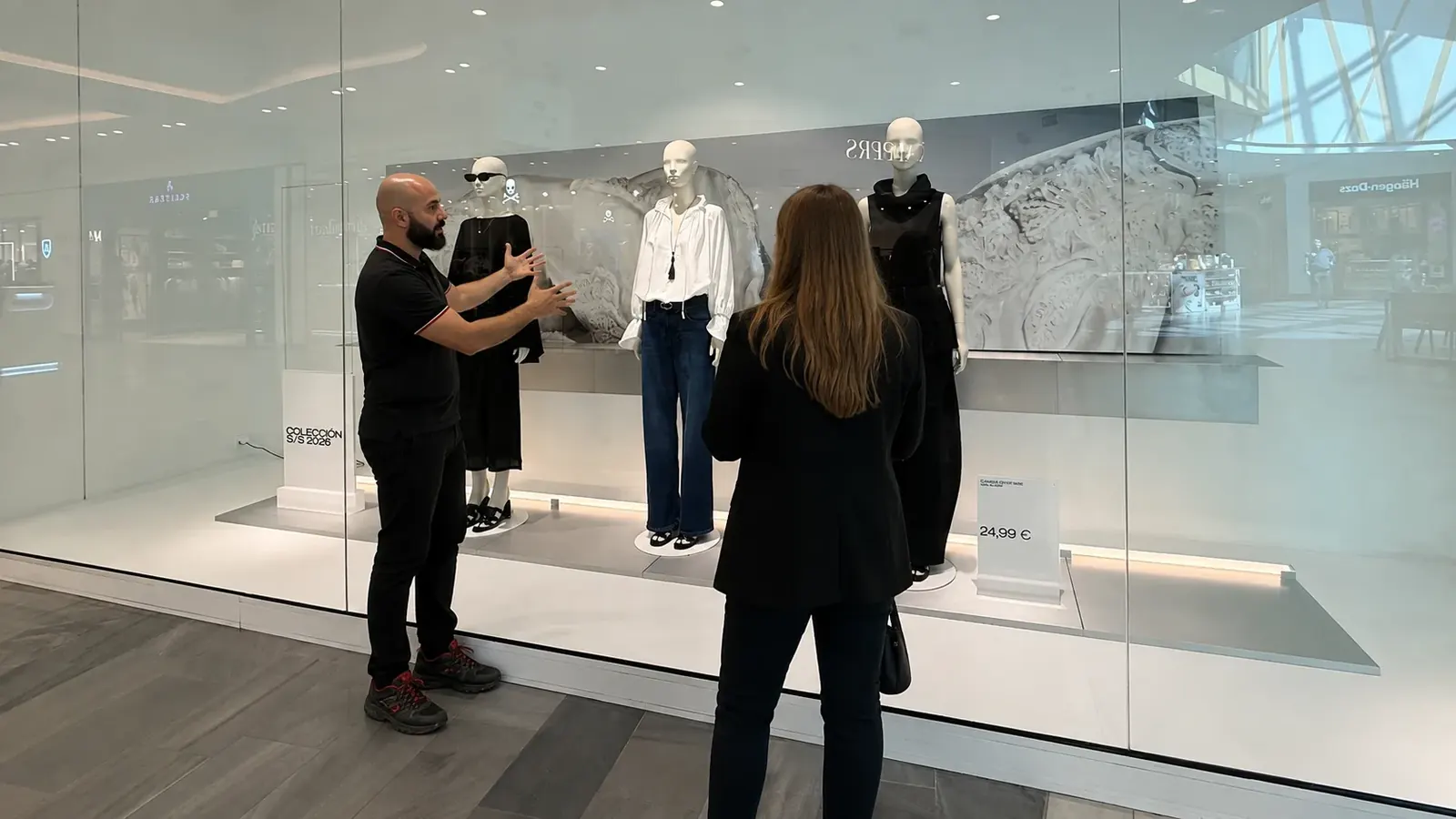 Visual merchandiser explicando a una clienta el montaje de un escaparate con maniquíes en una tienda de moda
