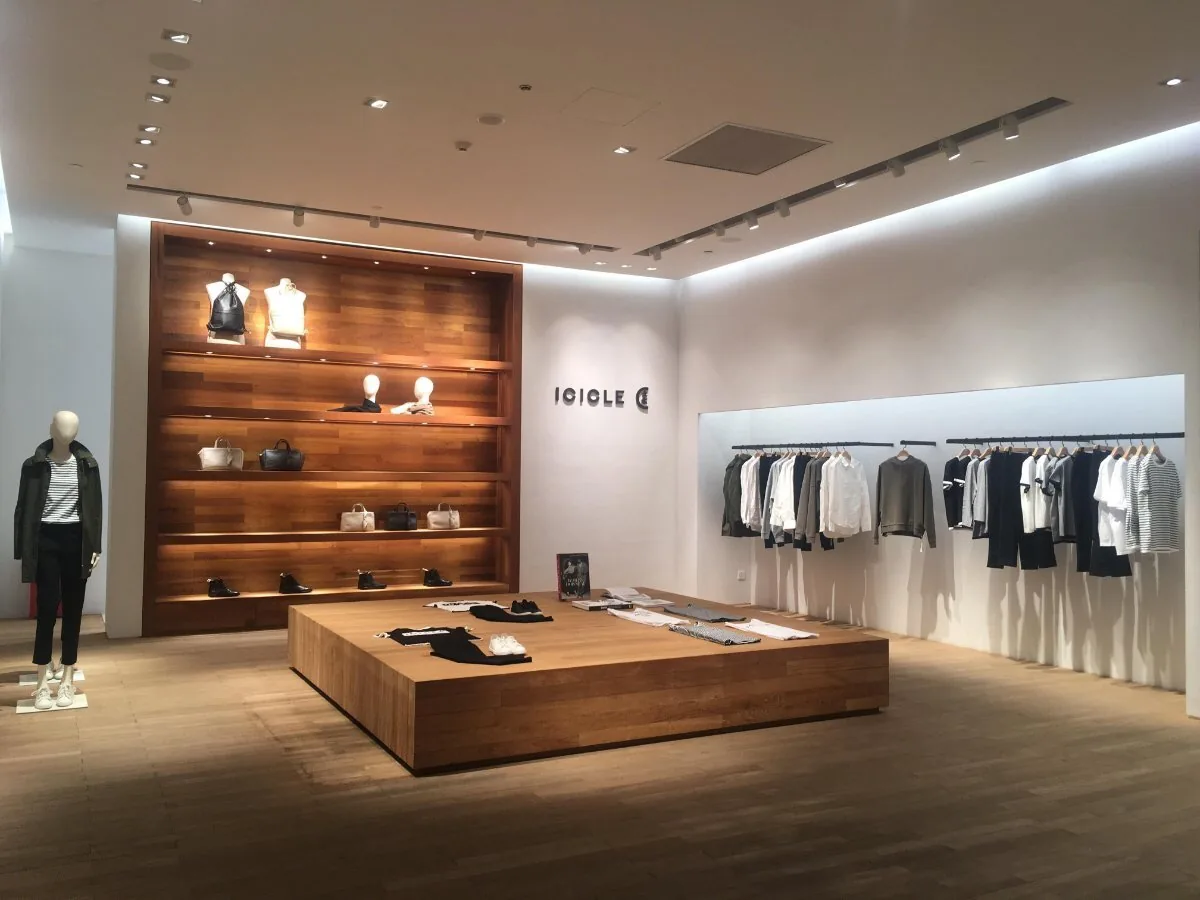 Tienda de moda recién implantada con mesa central de madera, estantería con producto doblado y maniquíes junto a la entrada